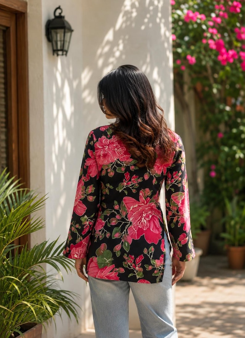 May include: Black floral print long-sleeve top with large pink flowers and green leaves. The top is worn with light blue jeans. The floral pattern is a striking contrast against the black background.