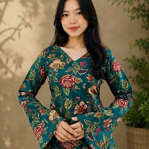 May include: A teal floral print top with long sleeves and a V-neck. The top features a vibrant pattern of red, yellow, and green flowers and leaves. The sleeves have a flared design. The top is made of a soft, flowing fabric.