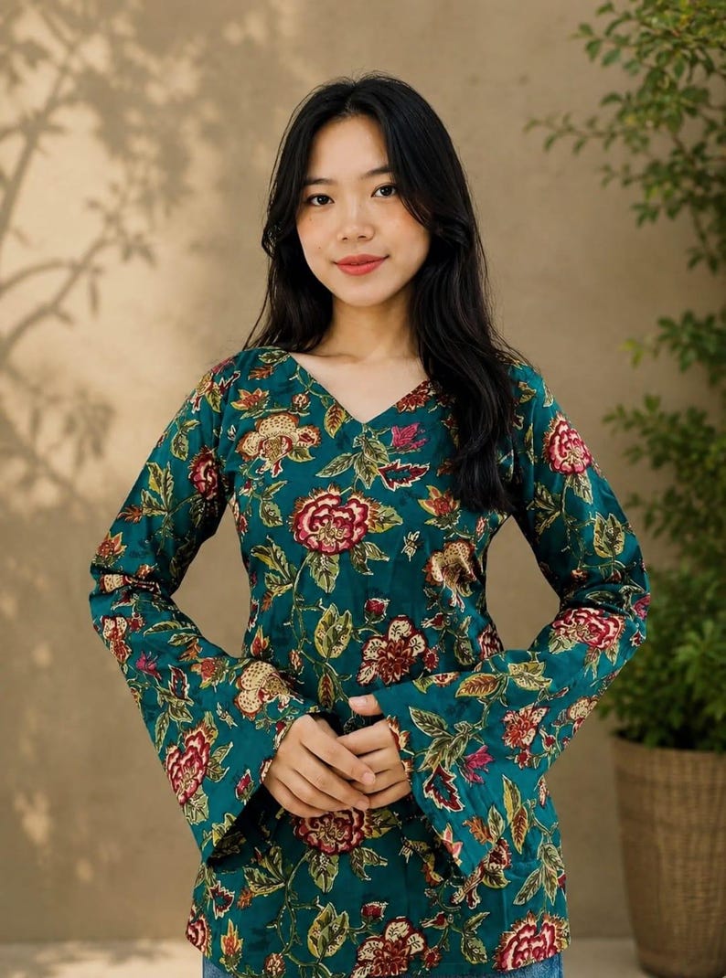 May include: A teal floral print top with long sleeves and a V-neck. The top features a vibrant pattern of red, yellow, and green flowers and leaves. The sleeves have a flared design. The top is made of a soft, flowing fabric.