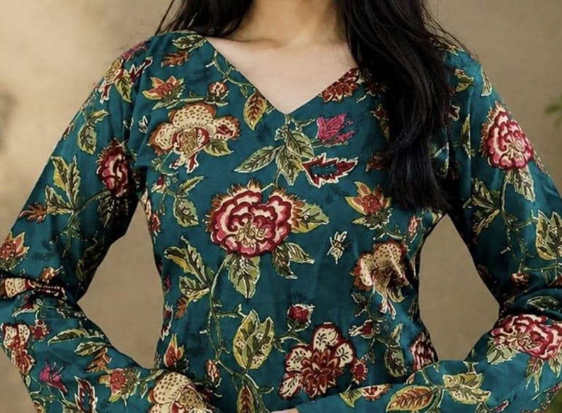 May include: Teal-colored top with a V-neck and long sleeves, adorned with a floral pattern in shades of red, cream, and green. The fabric appears to be a soft, flowing material, suitable for casual wear.