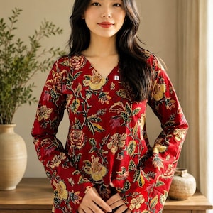May include: A long-sleeved, V-neck blouse in a vibrant red hue, adorned with a floral pattern in yellow, green, and brown. The blouse features a small 'S' tag and is made of a soft, flowing fabric. The floral design creates a classic, feminine look.