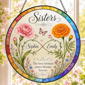 May include: Round stained glass window art with the word "Sisters" at the top. Features pink and orange flowers, a butterfly, and the names "Sophia" and "Emily". The text "The love between sisters blooms forever" is at the bottom.