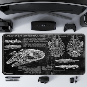May include: Black desk mat featuring a blueprint design of the Corellian YT-1300 Light Freighter (Modified). The mat includes detailed schematics and technical drawings in white against a black background. Other items on the desk include a monitor, speakers, and a gaming controller.