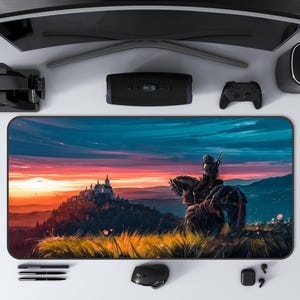 Könnte beinhalten: Rechteckige Schreibtischunterlage mit einer Fantasy-Landschaft, die ein Schloss, einen Reiter auf einem Pferd und einen Sonnenuntergang zeigt. Die Unterlage ist von Computerzubehör umgeben, darunter ein Monitor, Lautsprecher und eine Maus.