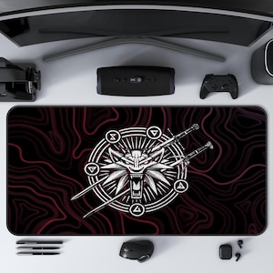 May include: A rectangular mouse pad with a red and black wavy pattern. The pad features a white wolf head emblem with crossed swords and geometric symbols. A computer mouse, pens, and other tech accessories surround the pad.