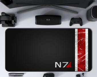 May include: Black rectangular mousepad with a red and white stripe on the right side and the letters "N7" in white. The mousepad is surrounded by a computer monitor, a speaker, a game controller, a mouse, and other tech accessories.