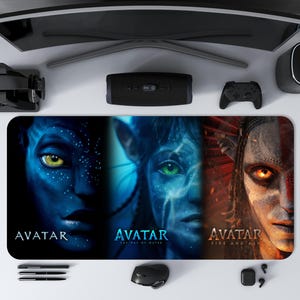 Könnte beinhalten: Ein rechteckiges Mauspad mit drei Gesichtern aus dem Film Avatar. Die Gesichter sind von blauhäutigen Na'vi-Charakteren mit auffälligen gelben und grünen Augen. Das Mauspad trägt die Filmtitel "Avatar", "Avatar: The Way of Water" und "Avatar: Fire and Ash".