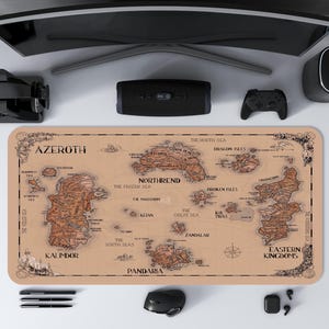 May include: A tan mousepad featuring a detailed map of Azeroth, with brown landmasses and text labels. The map includes regions like Kalimdor, Northrend, and Eastern Kingdoms. The mousepad is surrounded by computer accessories, including a monitor, speakers, and a game controller.