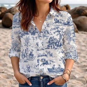 May include: A long-sleeved button-down shirt featuring a white base with a blue toile de jouy pattern depicting pastoral scenes with figures, horses, and boats. The shirt has a classic collar, a front button placket, and cuffed sleeves.