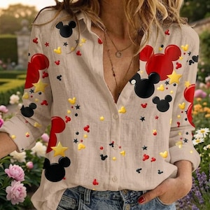 May include: A beige long-sleeve button-down shirt featuring a repeating pattern of red and black Mickey Mouse head silhouettes, yellow stars, and small red and yellow dots scattered across the fabric.