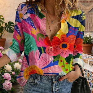 Op de afbeelding: Een overhemd met lange mouwen en knoopsluiting, voorzien van een levendige, veelkleurige bloemenprint met grote roze, rode, gele en groene bloemen op een donkerblauwe achtergrond. Het overhemd heeft een kraag, knoopsluiting en manchetten.