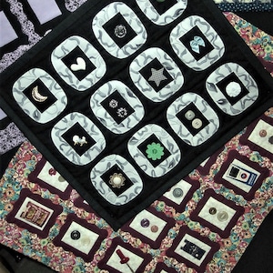 May include: A black fabric quilt with white and gray squares. Each square has a different button in the center. The quilt is made up of 16 squares.