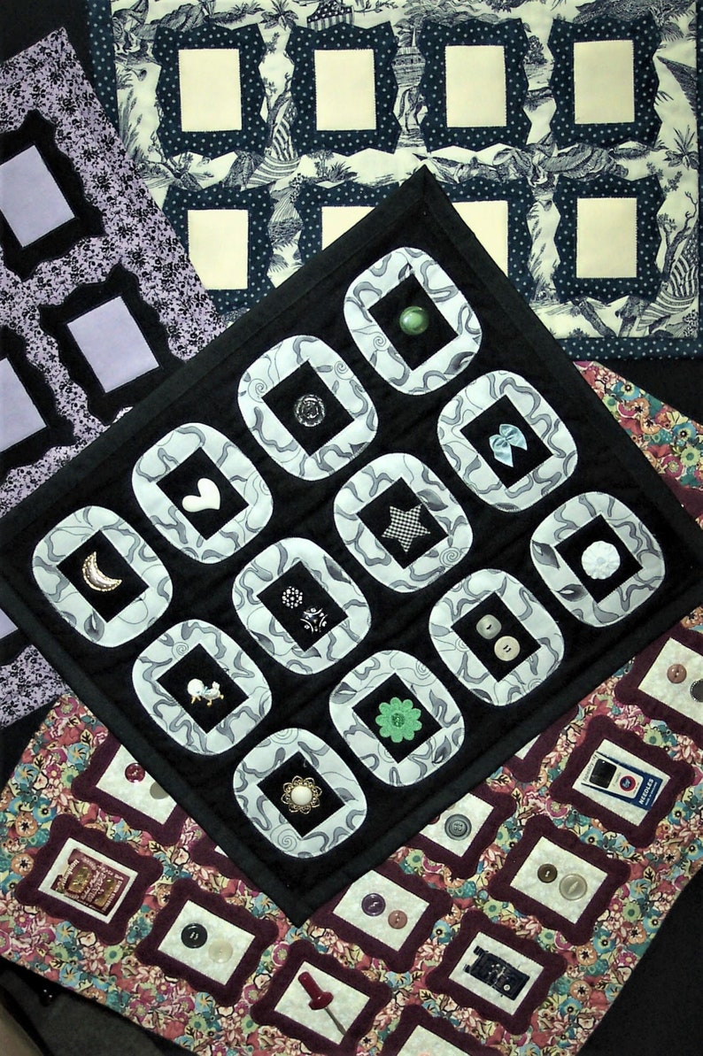 May include: A black fabric quilt with white and gray squares. Each square has a different button in the center. The quilt is made up of 16 squares.