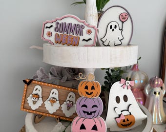 May include: A white, two-tiered tray decorated with Halloween-themed wooden cutouts. The decorations include ghosts, pumpkins, and a sign that reads "Summerween". The tray is set on a woven basket.