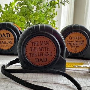 Puede incluir: Tres cintas métricas negras con etiquetas de cuero marrón. Las etiquetas tienen mensajes personalizados para papá, abuelo y "El hombre, el mito, la leyenda papá".