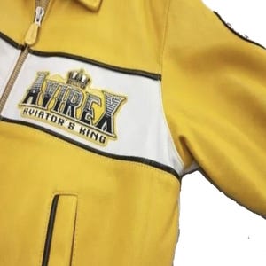 以下が含まれることがあります： 胸に「AVIREX AVIATOR'S KING」の文字が入ったワッペンが付いた、黄色と白のジャケット。 ジャケットはジッパー開閉式で、襟が付いています。 ジャケットは滑らかな素材で作られています。