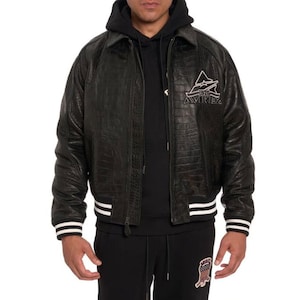 May include: Black leather jacket with a crocodile skin texture. The jacket has a zipper closure, a collar, and white stripes on the cuffs and hem. The Avirex logo is embroidered on the chest.