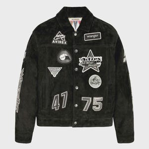 Puede incluir: Una chaqueta de ante negro con cierre de botones, cuello en punta y mangas largas. La parte delantera est&aacute; decorada con varios parches bordados, incluyendo el texto Avirex, Wrangler y los n&uacute;meros 47 y 75 en blanco y gris.