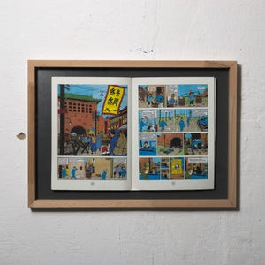 Könnte beinhalten: Gerahmte Comic-Seiten mit farbenfrohen Illustrationen einer Stadtszene mit Personen in blauer Kleidung. Die Kunstwerke sind im klassischen Comic-Stil gehalten, mit Sprechblasen und Panels.