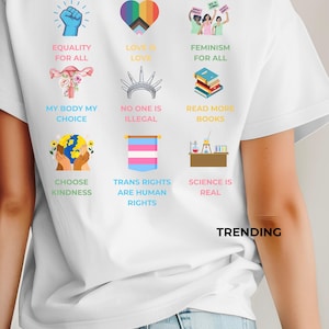 Könnte beinhalten: Weißes T-Shirt mit bunten Grafiken und Texten, die Gleichberechtigung, Liebe, Feminismus und Menschenrechte fördern. Das Shirt zeigt die Sätze "Gleichheit für alle", "Liebe ist Liebe" und "Trending".