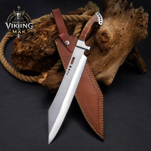 May include: A fixed-blade knife with a silver-toned steel blade featuring four circular cutouts near the hilt, a polished wooden handle with metal rivets, and a brown leather sheath with a snap closure and visible stitching along the edges.