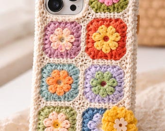 May include: A cream-colored crochet phone case featuring a colorful floral design. The case has a grid pattern of squares, each with a different colored flower in the center. The flowers are in shades of pink, orange, yellow, and blue. The case is designed to fit a smartphone.