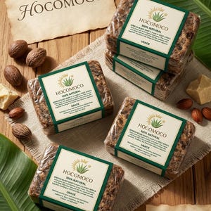 Può includere: Diverse saponette avvolte di sapone nero africano HOCOMOCO 100% naturale sono disposte su una superficie di legno con noci e una foglia. Ogni saponetta ha un'etichetta verde e bianca. L'immagine include anche il testo "High Quality Product".