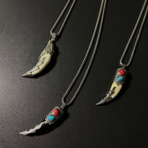 May include: Three silver-toned necklaces with pendant designs. One pendant is a stylized tooth with silver accents. The other two pendants are tooth-shaped with red and turquoise stones. The necklaces are on a black surface.