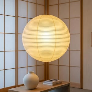 May include: A large, round paper lantern hangs from the ceiling, emitting a soft, warm glow. The lantern is made of horizontal strips of paper. Below, a white vase and books rest on a wooden table, set against a backdrop of traditional Japanese shoji screens.