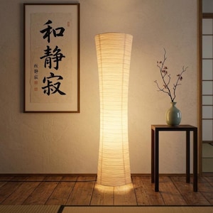 Könnte beinhalten: Eine hohe, cremefarbene Stehlampe mit einem zylindrischen, strukturierten Schirm. Die Lampe beleuchtet einen Raum mit einem gerahmten Kunstwerk im asiatischen Stil und einem kleinen Beistelltisch mit einer Blumenvase.