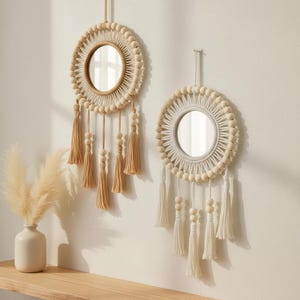 May include: Two round wall mirrors with a bohemian design. Each mirror features a circular frame adorned with wooden beads and tassels. The mirrors are hung on a white wall, with a vase of pampas grass on a wooden shelf.