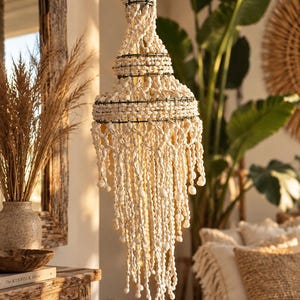 Peut inclure: Un luminaire suspendu à plusieurs niveaux composé d'une structure en métal foncé ornée de nombreuses petites coquilles blanc cassé. L'objet présente une partie supérieure effilée et plusieurs rangées de coquillages en cascade.