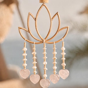 Op de afbeelding: Decoratieve wandhanger met een lotusbloemdesign gemaakt van lichtbruin bamboe. De bloem heeft vijf bloembladen en is versierd met strengen houten kralen, schelpen en roze hartvormige stenen. Een natuurlijke, bohemien stijl.