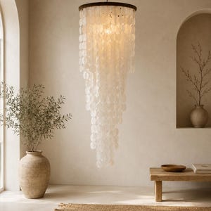 Peut inclure: Un lustre à étages composé de nombreux disques translucides en nacre blanche circulaire, suspendus à un cadre circulaire sombre. Le luminaire est accroché par une fine chaîne, formant une structure cylindrique en cascade diffusant une lueur douce.