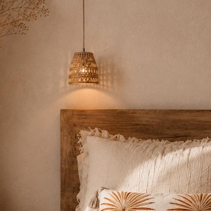 May include: A woven rattan pendant light hangs above a bed. The light fixture has a conical shape and a warm, inviting glow. The bed features a wooden headboard and white pillows with decorative palm tree embroidery.