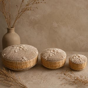 May include: Three round lidded boxes of varying sizes, each featuring a woven light brown base and a top surface covered in small cream-colored beads arranged in a floral pattern with white cowrie shells embedded in the center and edges.