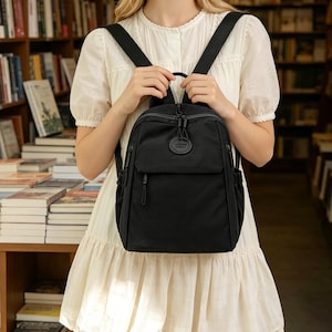 Peut inclure: Sac à dos noir avec plusieurs compartiments, dont une poche avant et des poches latérales. Il est doté de bretelles réglables et d'une poignée supérieure. Le design est épuré et minimaliste, adapté à un usage quotidien.
