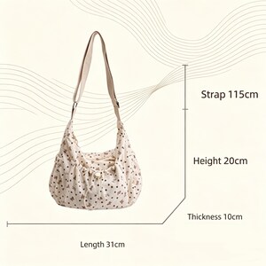 May include: Cream-colored shoulder bag with a floral pattern. The bag has a strap that is 45 inches long, a height of 8 inches, a length of 12 inches, and a thickness of 4 inches. The bag has a drawstring closure and a button.