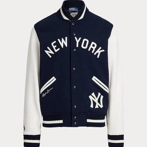 Può includere: Giacca college blu navy e bianca con la scritta "NEW YORK" a lettere bianche. La giacca ha maniche bianche, colletto e polsini a coste e un logo sul davanti.