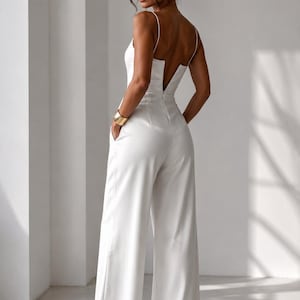 Op de afbeelding: Een effen witte jumpsuit met een mouwloos lijfje met dunne spaghettibandjes, een diepe V-hals aan de achterkant en een broek met wijde pijpen. Het kledingstuk is voorzien van zijzakken en een getailleerde pasvorm voor een strak silhouet.