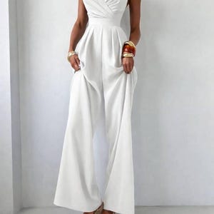 Op de afbeelding: Een effen witte jumpsuit met een hartvormige halslijn, dunne spaghettibandjes en een getailleerd lijfje met een geplooide taille. Het kledingstuk heeft een broek met wijde pijpen die tot op de grond valt, wat zorgt voor een strak en gestructureerd silhouet.