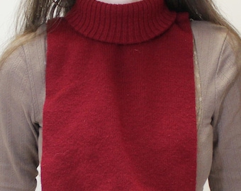May include: A deep red turtleneck collar, designed to be worn under clothing. The collar is made of a knitted material and has a ribbed texture on the turtleneck. The rectangular bib hangs down the chest.
