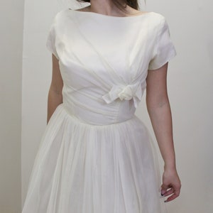 May include: A white vintage dress with a fitted bodice and a full skirt. The bodice has a bow detail at the neckline.