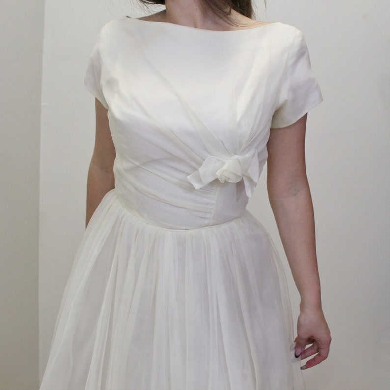 May include: A white vintage dress with a fitted bodice and a full skirt. The bodice has a bow detail at the neckline.