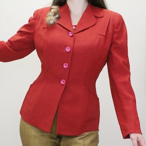 May include: A red blazer with a fitted waist and a row of pink buttons down the front. The blazer has a notched collar and long sleeves.