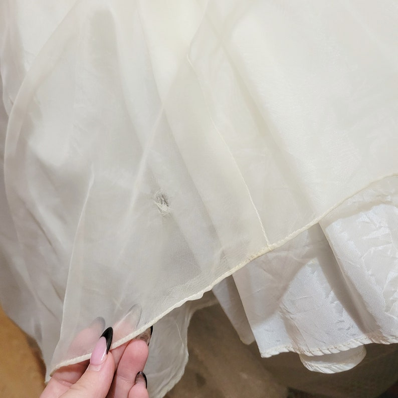May include: Close-up of a white tulle fabric with a small hole in the center. The fabric is layered and has a delicate texture.