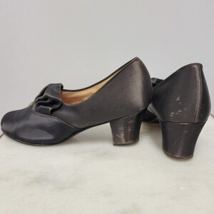 May include: A pair of vintage dark brown satin pumps with a small heel. The shoes feature a decorative ruffle detail on the vamp. The heels show signs of wear. The shoes are likely from the early to mid-20th century.