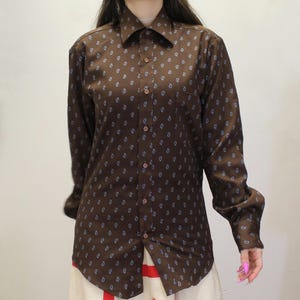 May include: A brown button-down shirt with a paisley pattern in light blue. The long-sleeved shirt has a classic collar and buttoned cuffs. The shirt is made of a smooth fabric.