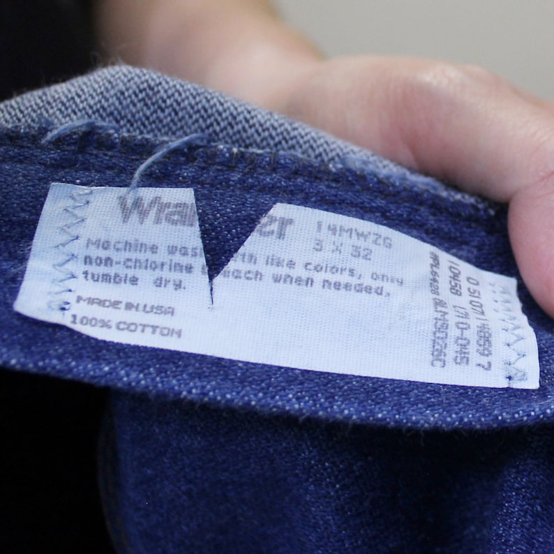 May include: A blue denim label with white text that reads "Machine wash with like colors, only bleach when needed. Made in USA 100% Cotton" and "14MWZG 3X32".