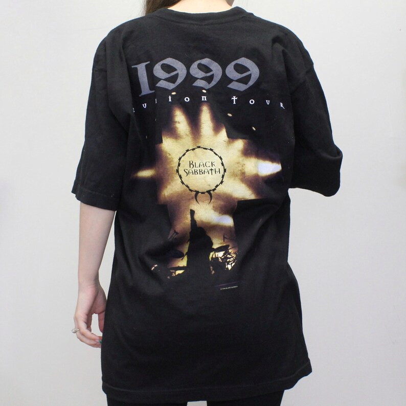 May include: Black t-shirt with a graphic print of a cross with the text "1999 Reunion Tour" and "Black Sabbath" in a circle.